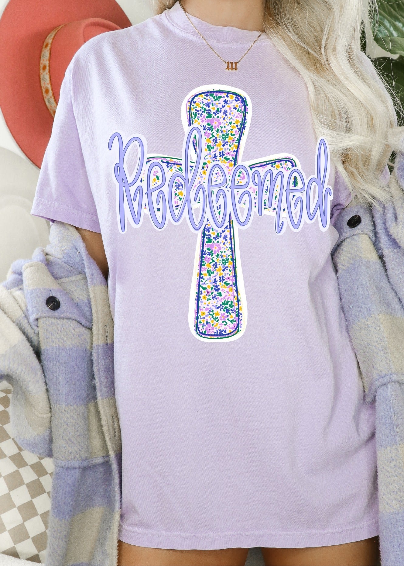 Person wearing a light purple t-shirt with a floral cross design and 'Redeemed' text.