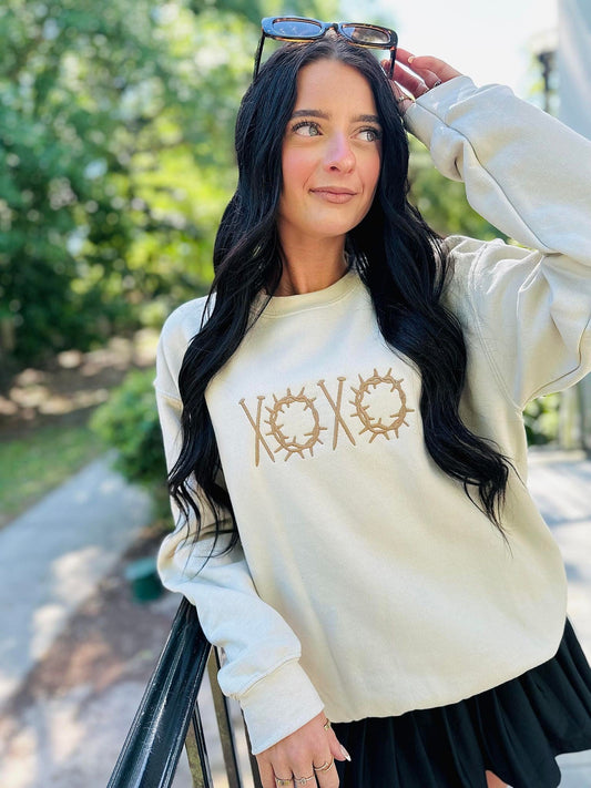 Woman wearing a cream-colored sweatshirt with 'XOXO' design outdoors.