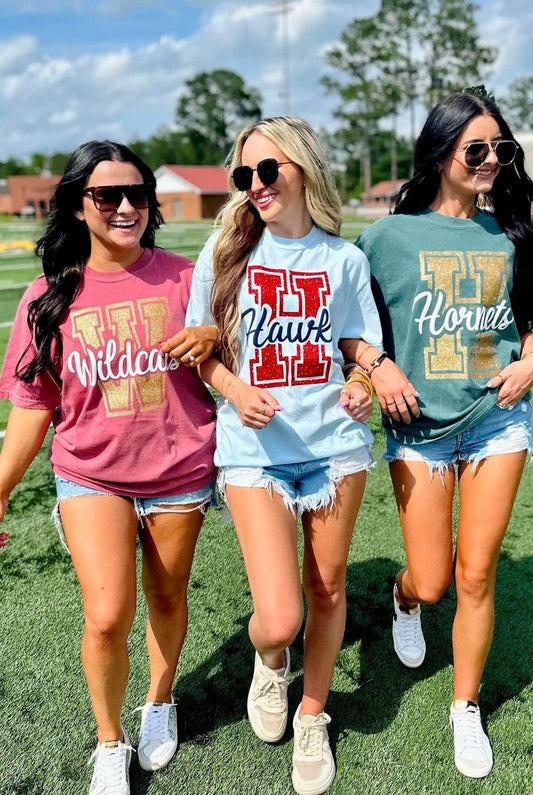 Three women wearing school spirit shirts on a sports field