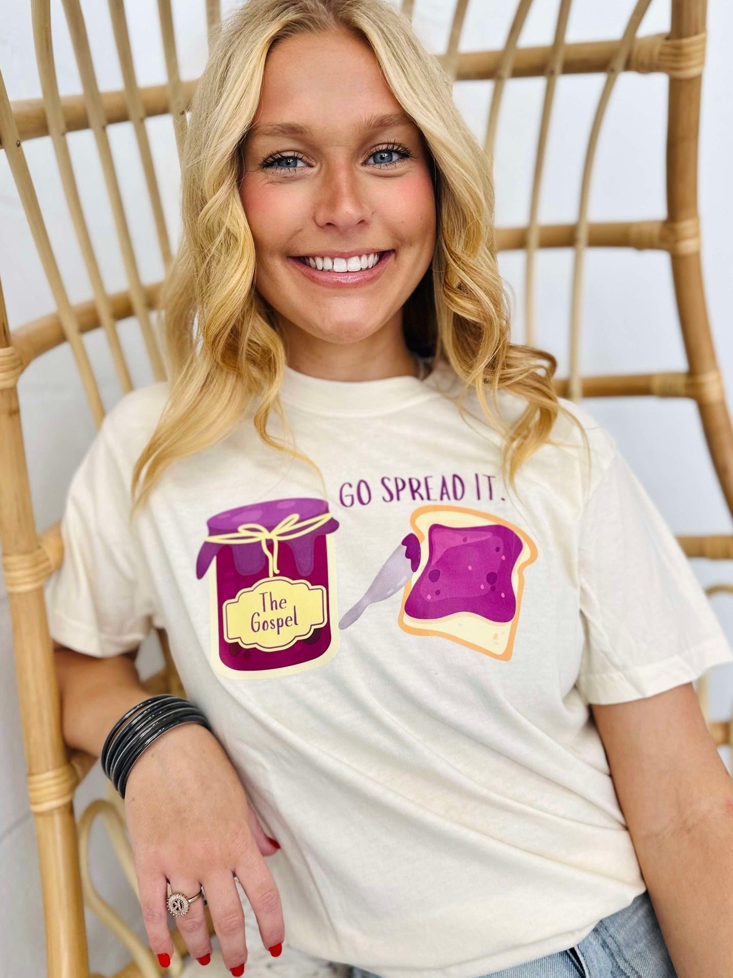 Person wearing a white t-shirt with graphics and text "Go spread it", sitting on a wicker chair.