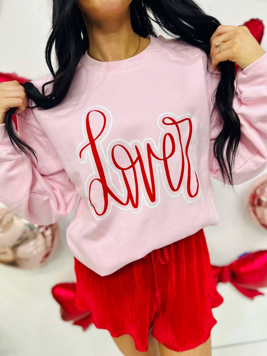 Person wearing a pink sweatshirt with 'Lover' written in red, standing against a white background.