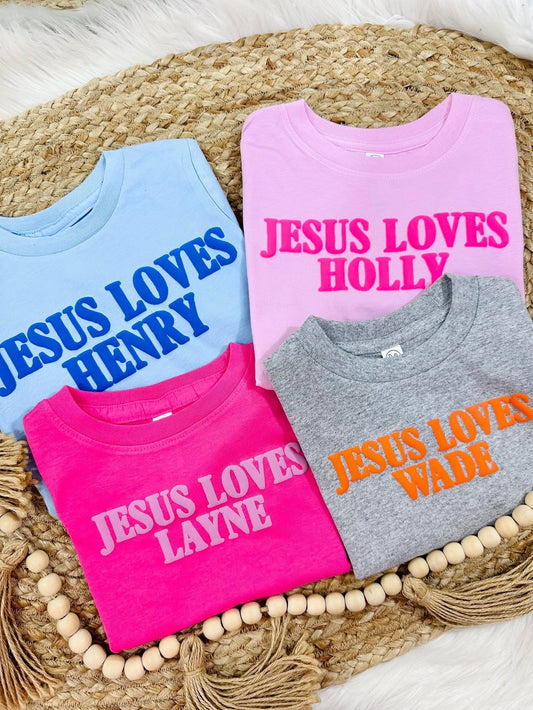 Four children's sweatshirts with Jesus Loves personalized names on a woven mat.