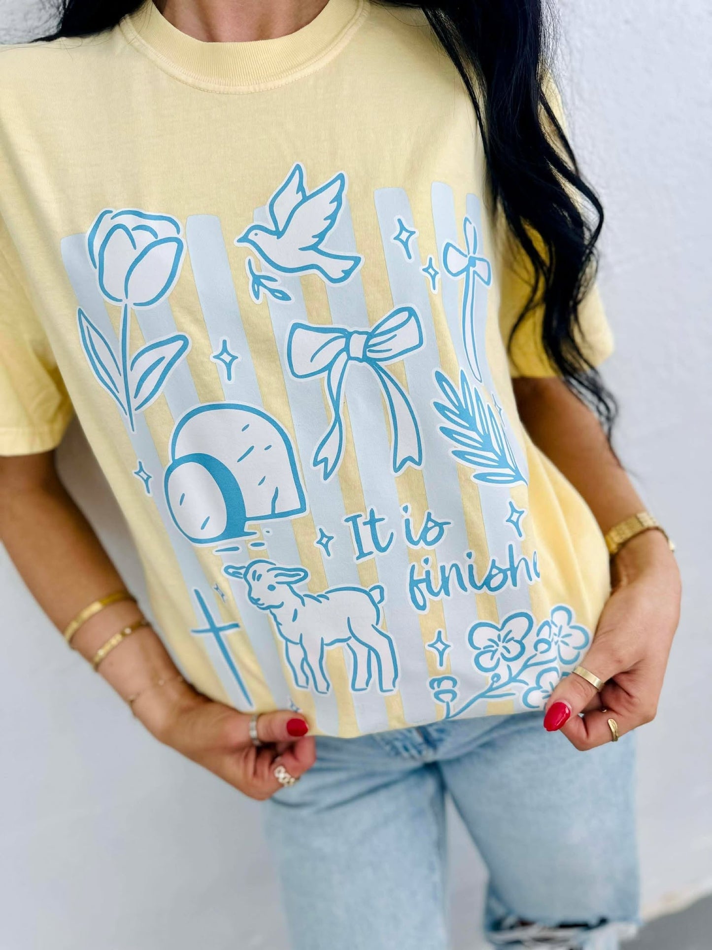 Person wearing a yellow t-shirt with blue illustrations and IT IS FINISHED text.
