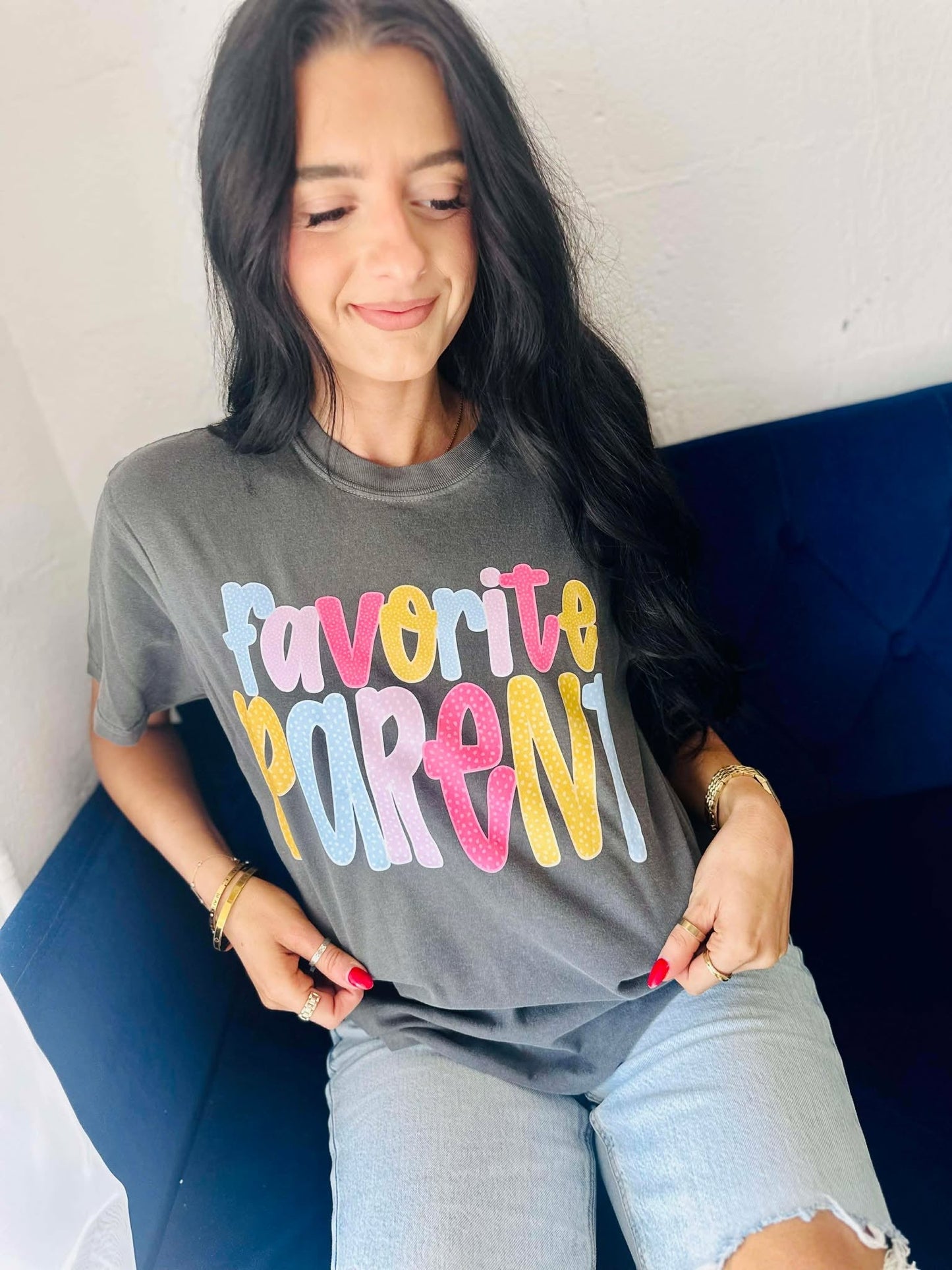 Woman wearing a gray t-shirt with 'Favorite Parent' in polka dot colorful letters, sitting on a blue couch.