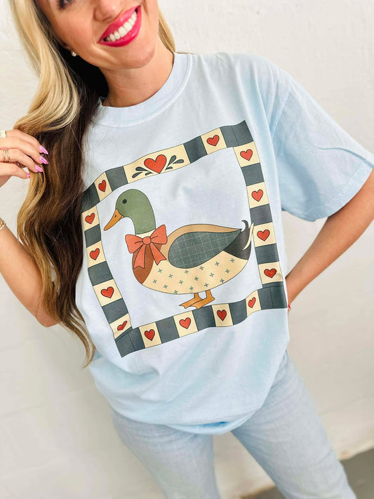 Woman wearing a light blue t-shirt with a duck mallard patchwork graphic design.