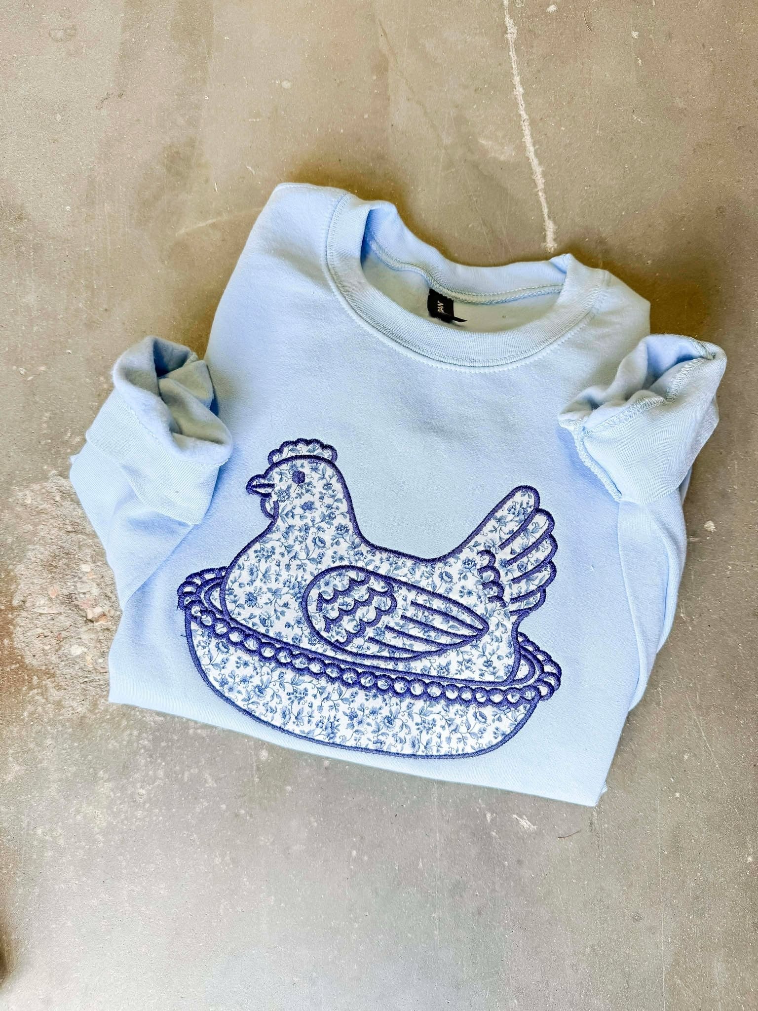 White sweatshirt with blue graphic design on a beige surface