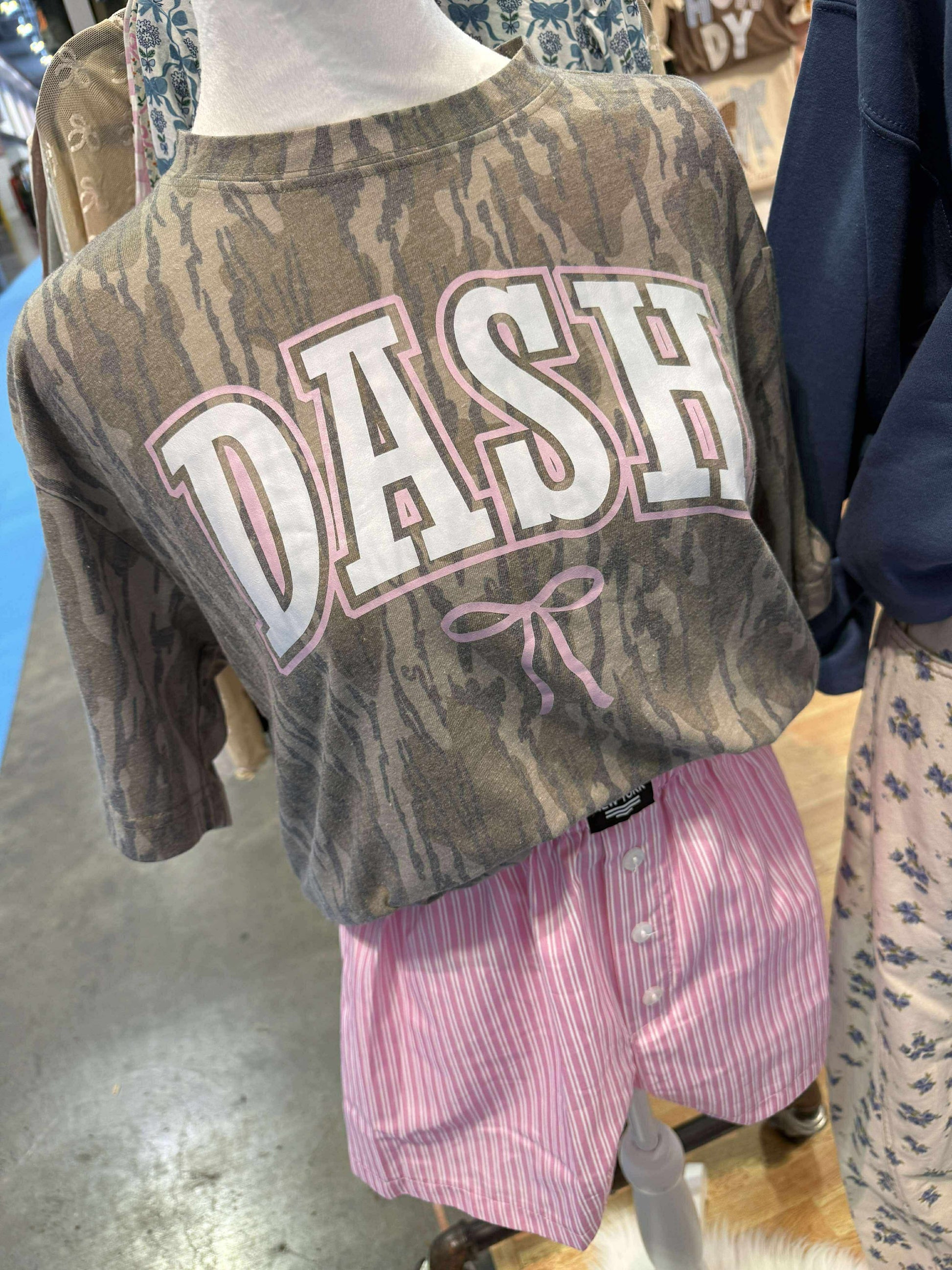 Bottomland Mossy Oak Camouflage sweatshirt with 'DASH' text and a bow on a mannequin in a store setting.