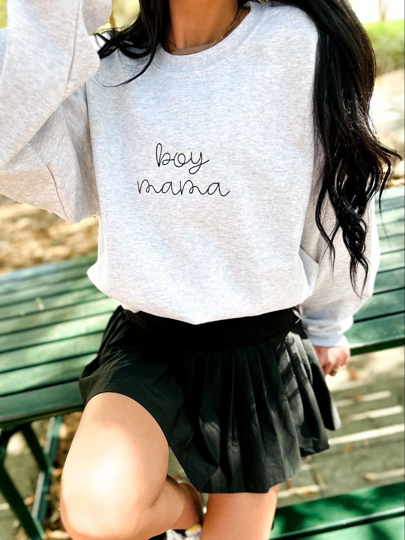 Child wearing a gray sweatshirt with 'boy mama' text, sitting on a green bench.