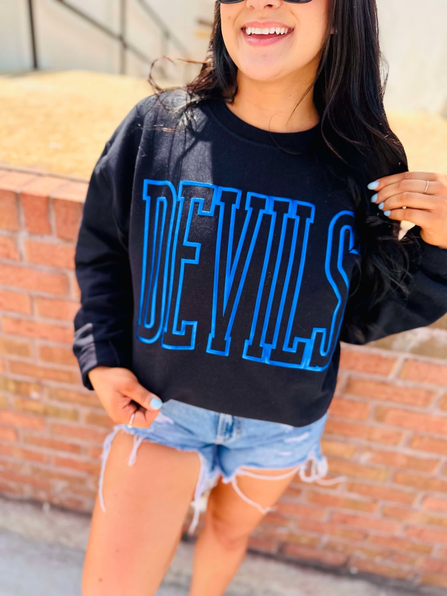 Person wearing a black sweatshirt with 'DEVILS' in blue letters against a brick wall.