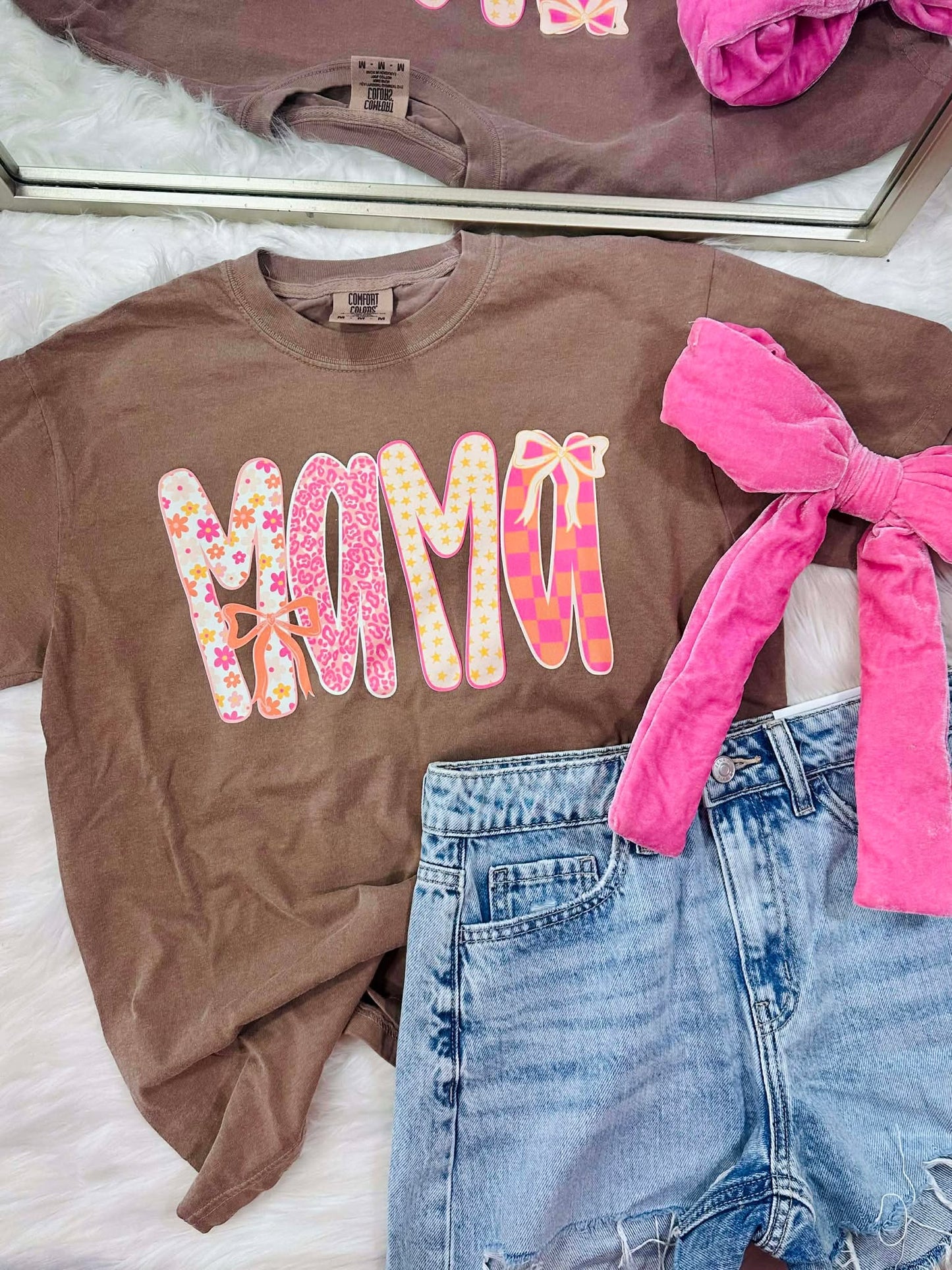 Brown t-shirt with 'MAMA' print, pink shorts, and denim shorts on a white surface.