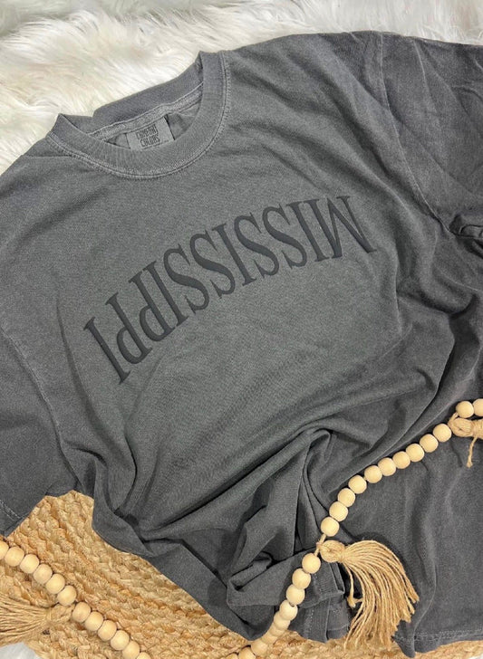 Gray t-shirt with 'MISSISSIPPI' printed on it, draped over a textured surface.